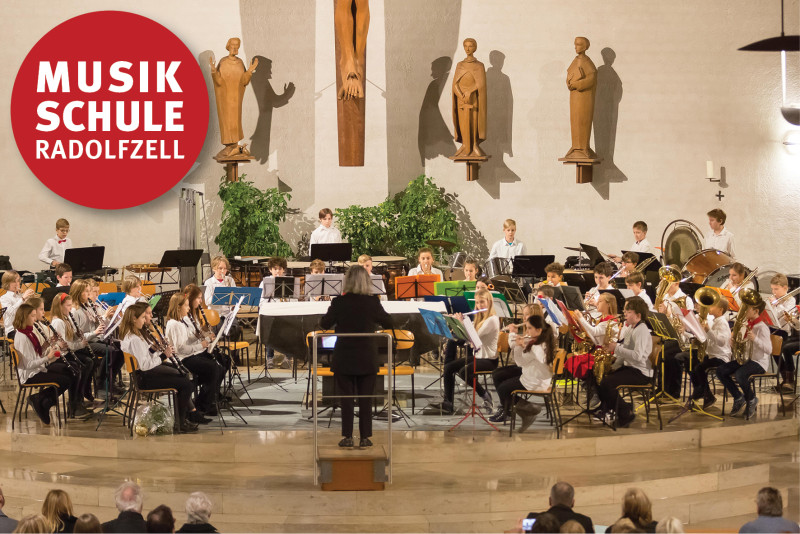 Musikschule Radolfzell: Orchester mit Dirigentin bei einem Konzert. Musiker spielen Instrumente.