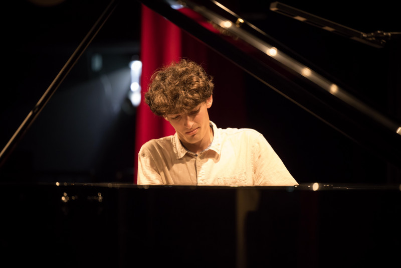 Junger Pianist spielt Klavier auf der Bühne. Konzert, Musik, Künstler.